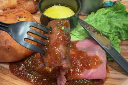 ユニバーサル・スタジオ・ジャパンのモンスターハンターワイルズ・コラボプレート。フォークで持ち上げた厚切りローストビーフのシズル感あふれるアップ。