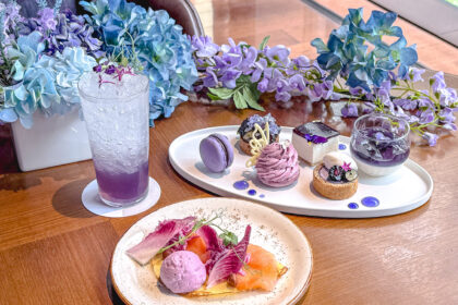 ハイアット セントリック 銀座 東京の、紫と青のアジサイや藤の花に彩られたテーブルに並ぶ、紫色のスイーツプレート、ドリンク、セイボリーのアフタヌーンティーセット。