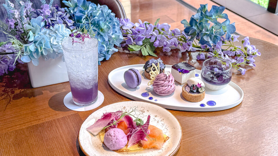 ハイアット セントリック 銀座 東京の、紫と青のアジサイや藤の花に彩られたテーブルに並ぶ、紫色のスイーツプレート、ドリンク、セイボリーのアフタヌーンティーセット。
